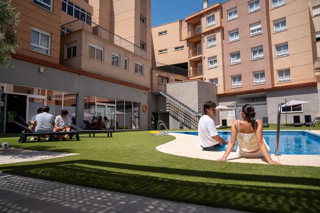 Dos residentes charlando sentados al borde de la piscina, con el edificio de la residencia al fondo